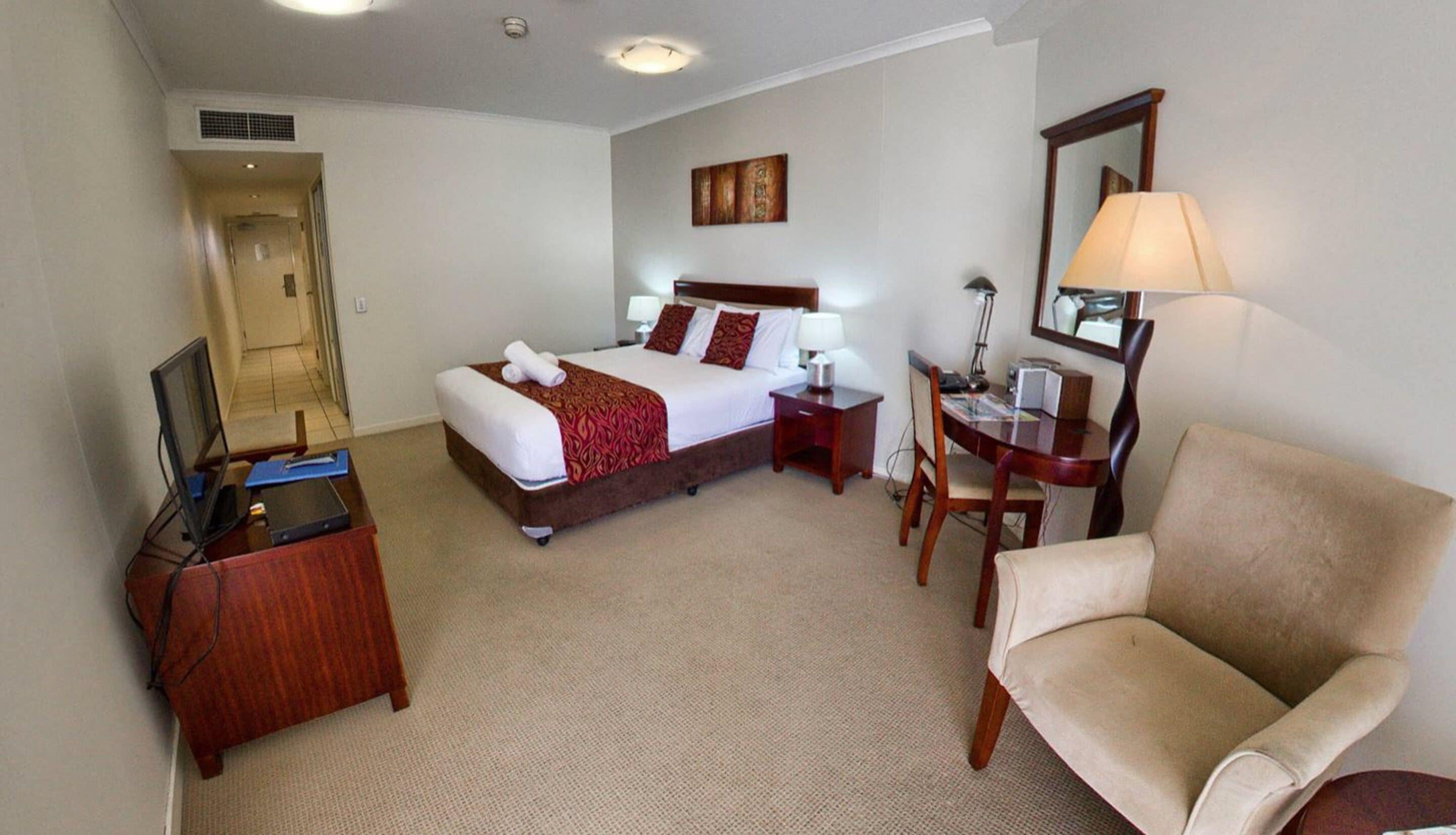 A hotel room with a bed, a desk, a chair, a TV, and a door.