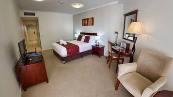 A hotel room with a bed, a desk, a chair, a TV, and a door.