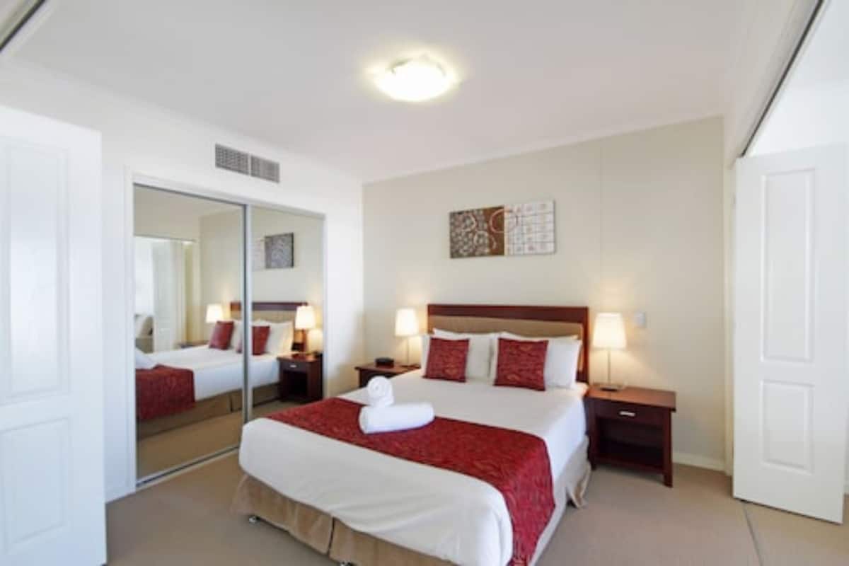 A hotel room with a large bed, two bedside tables, a mirror, and a wall-mounted artwork.