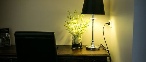 Ein Schreibtisch mit Lampe und Blumen in einer Vase, ein Stuhl und eine Steckdose.