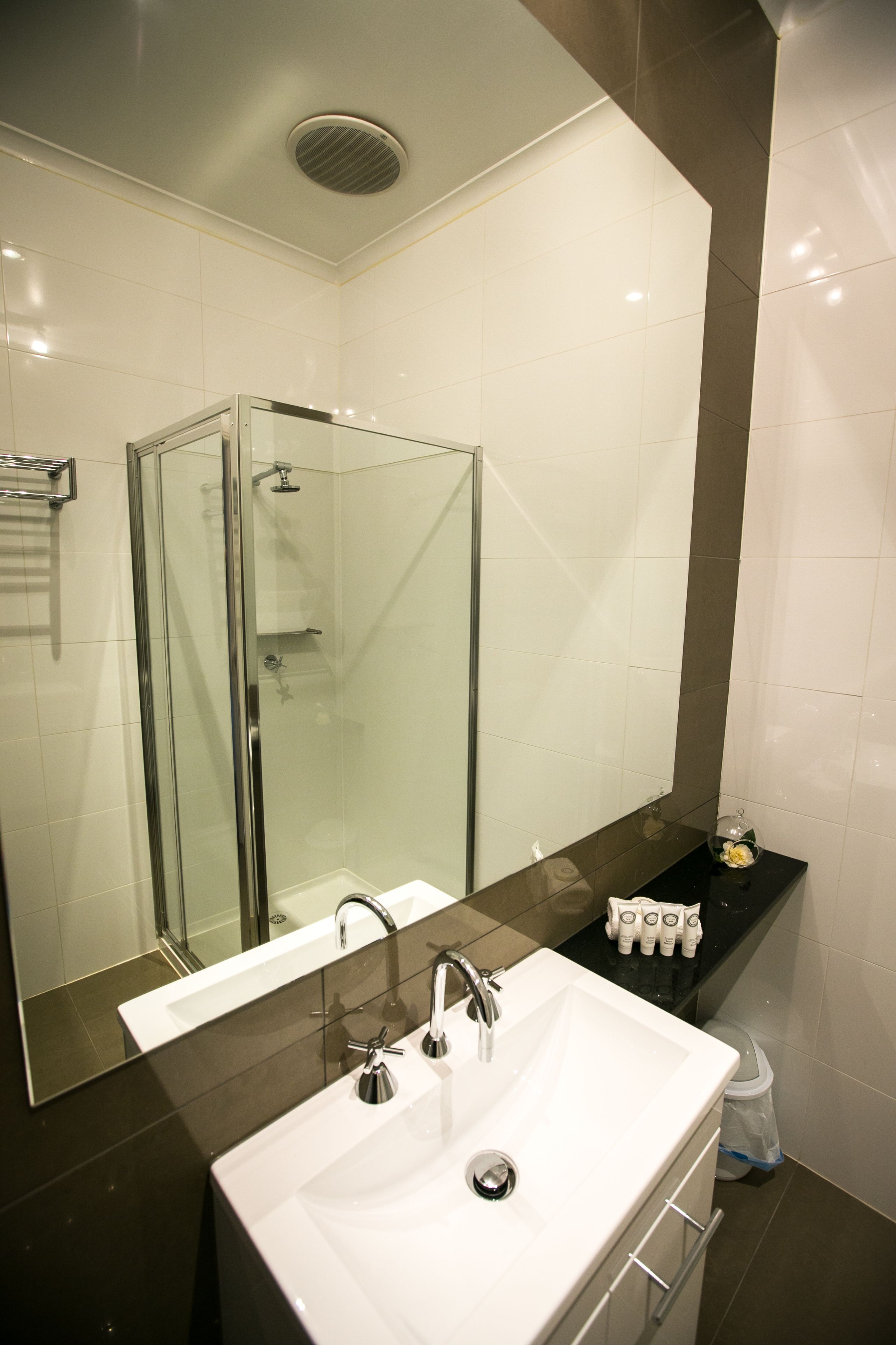 Een moderne badkamer met een douchecabine van glas, een witte wastafel en een spiegel erboven.