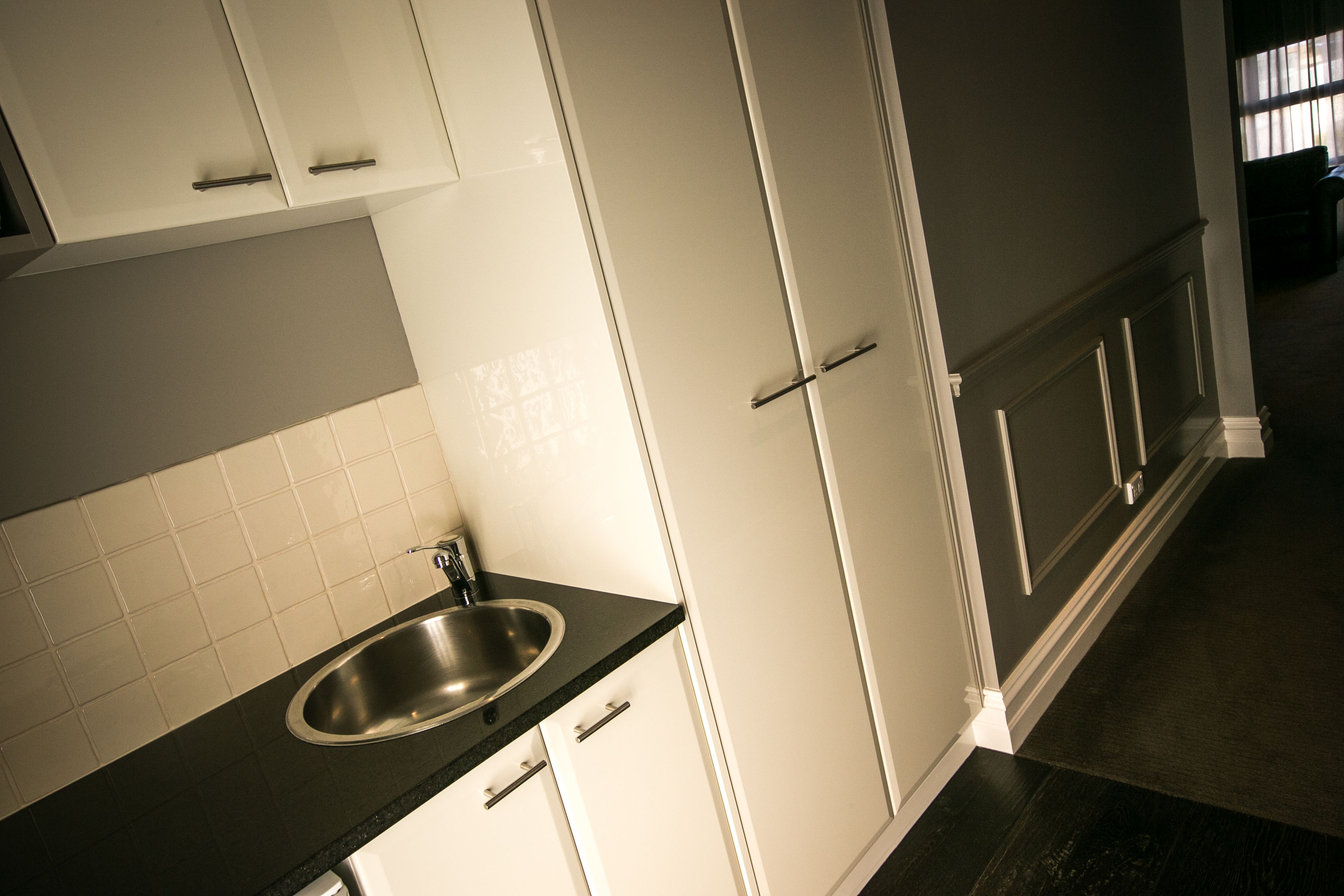 Een keuken met witte kasten, een roestvrijstalen spoelbak en een donker aanrecht.