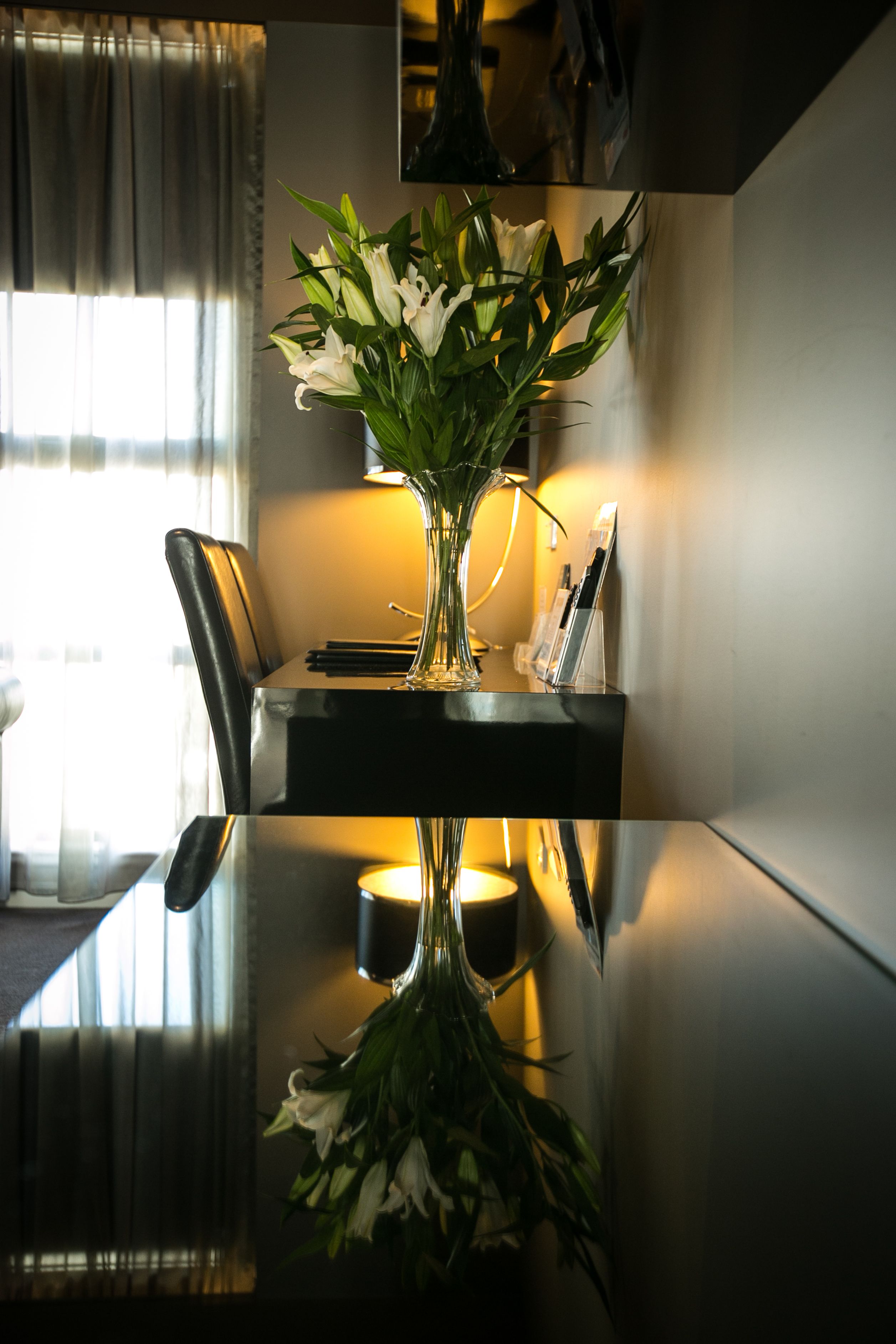 A dining table with a vase of white flowers, a lamp, and a magazine holder.