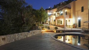 A multi-story building with a pool, stone walls, and outdoor lighting. - Kastellos Village (Georgioupolis)