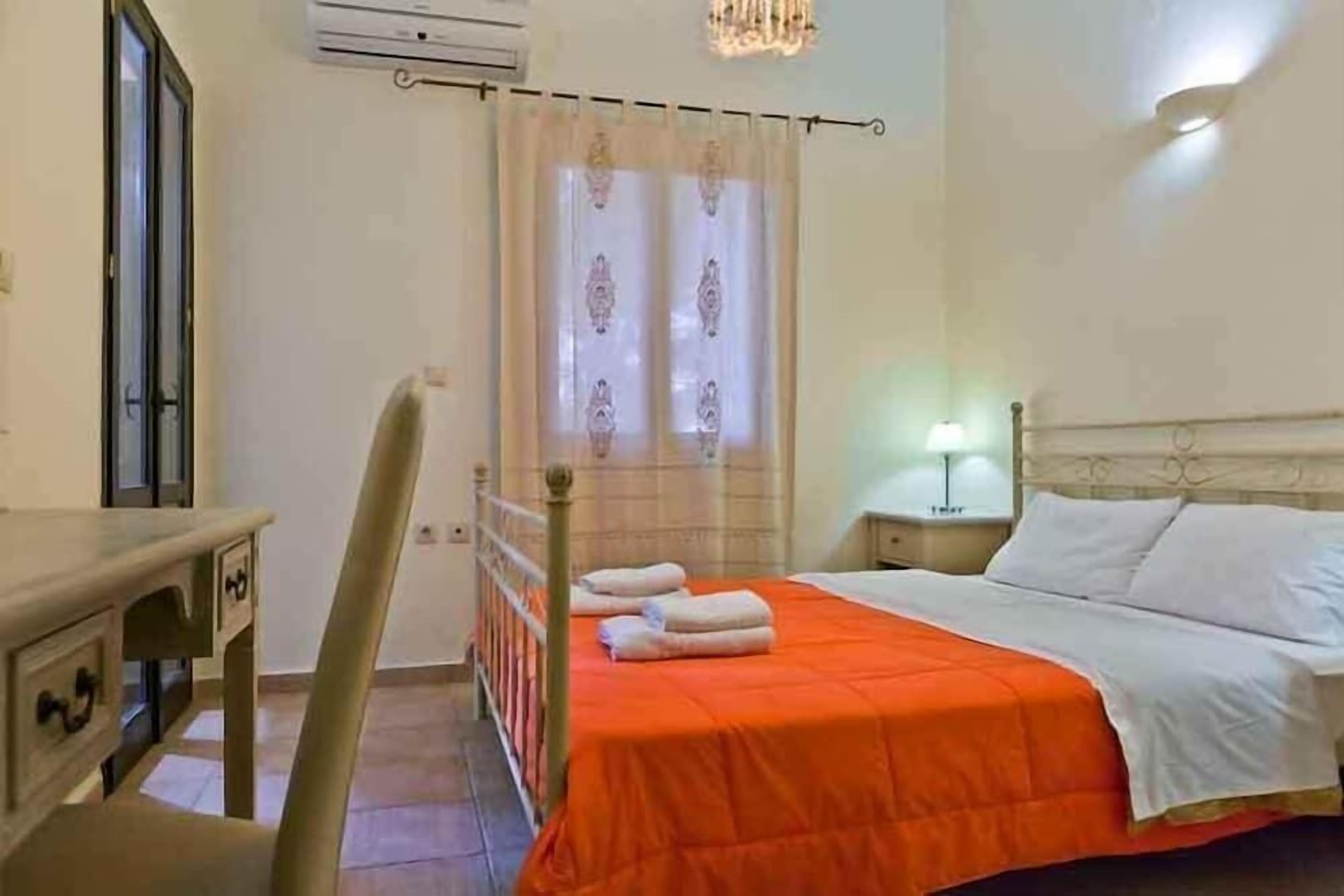 A bedroom with a bed, a desk, a chair, a nightstand, and a window with curtains.