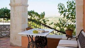 A covered outdoor seating area with a table and chairs, a bench, and a view of the landscape. - Kastellos Village (Georgioupolis)