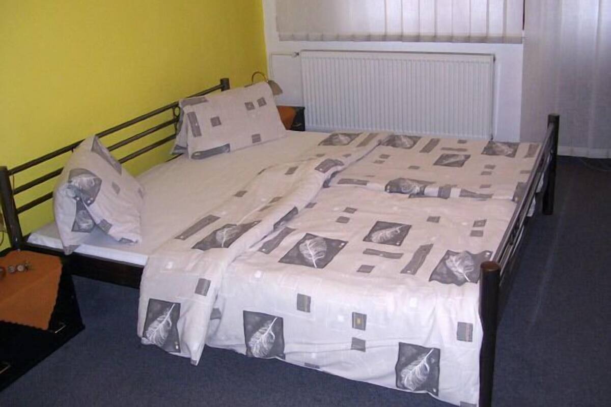 A single bed with a patterned bedspread in a room with yellow walls and a radiator.