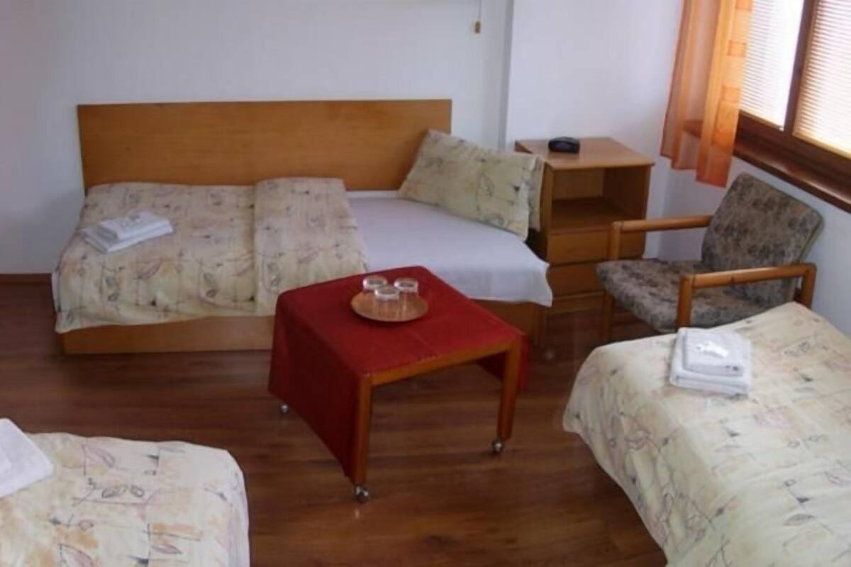 A small, cozy room with a wooden bed, a single chair, and a small table with a red cloth.