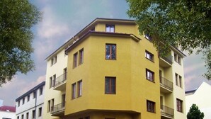 A yellow multi-story building with balconies, a parking lot, and adjacent buildings.
