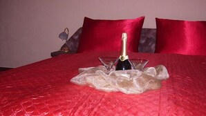 A bed with a red bedspread, a bottle of champagne, and two glasses on it.