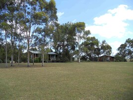A grassy field with trees and a house in the background.