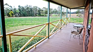 Un espace extérieur abrité, doté d’une terrasse en bois, d’une rambarde en métal et d’une table avec des chaises.