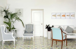 A room with a white door, a white sofa, a striped chair, and a table with chairs. There are framed pictures on the wall. - Sina Flora Capri (Capri)