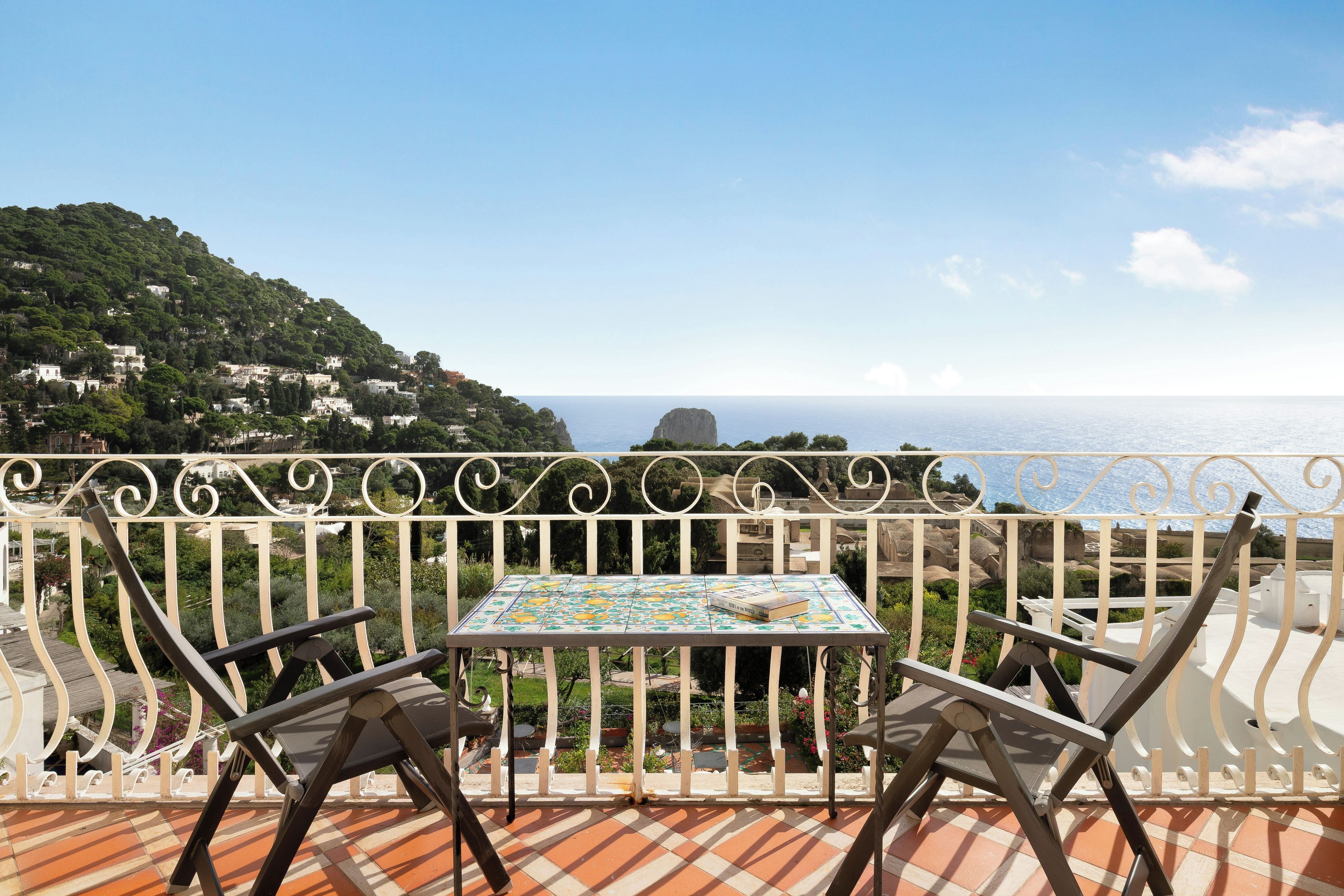 Una terraza con mesa y sillas, con vistas a un paisaje costero con edificios y una destacada formación rocosa.