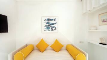 Quarto com cama, almofadas amarelas, uma obra de arte de peixes na parede e uma prateleira com objetos decorativos.