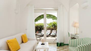 A room with a white sofa, a striped chair, a small table, and a view of an outdoor patio with chairs and a table.