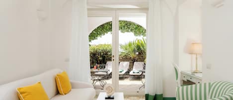 A room with a white sofa, a striped chair, a small table, and a view of an outdoor patio with chairs and a table.