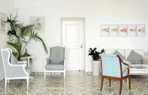 A room with a white door, a white sofa, a striped chair, and a table with chairs. There are framed pictures on the wall.