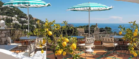 Un patio al aire libre con sombrillas a rayas, mesas, sillas y limoneros.