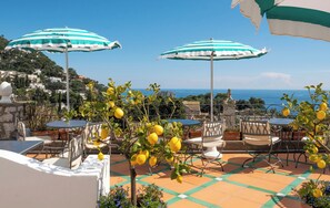 Un patio al aire libre con sombrillas a rayas, mesas, sillas y limoneros.