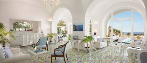 Amplia sala de estar con muebles blancos, piso de baldosas y grandes ventanales con vistas.