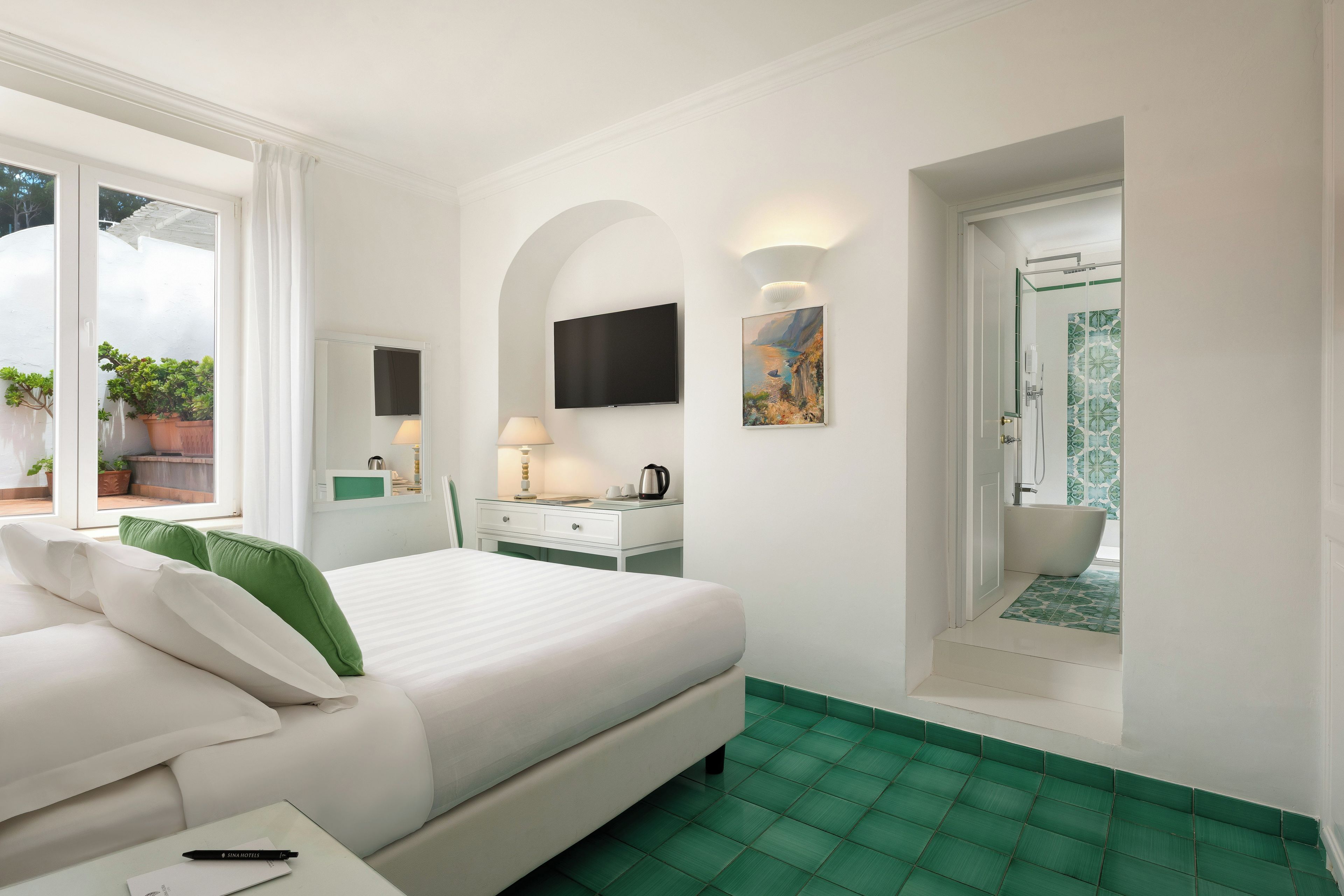 A hotel room with a bed, a desk, a TV, a painting, and a bathroom with a shower and bathtub.