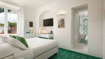 A hotel room with a bed, a desk, a TV, a painting, and a bathroom with a shower and bathtub.