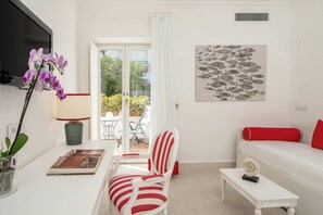 A modern living room with a sofa, a chair, a small table, a TV, and a door leading to an outdoor area. - Sina Flora Capri (Capri)