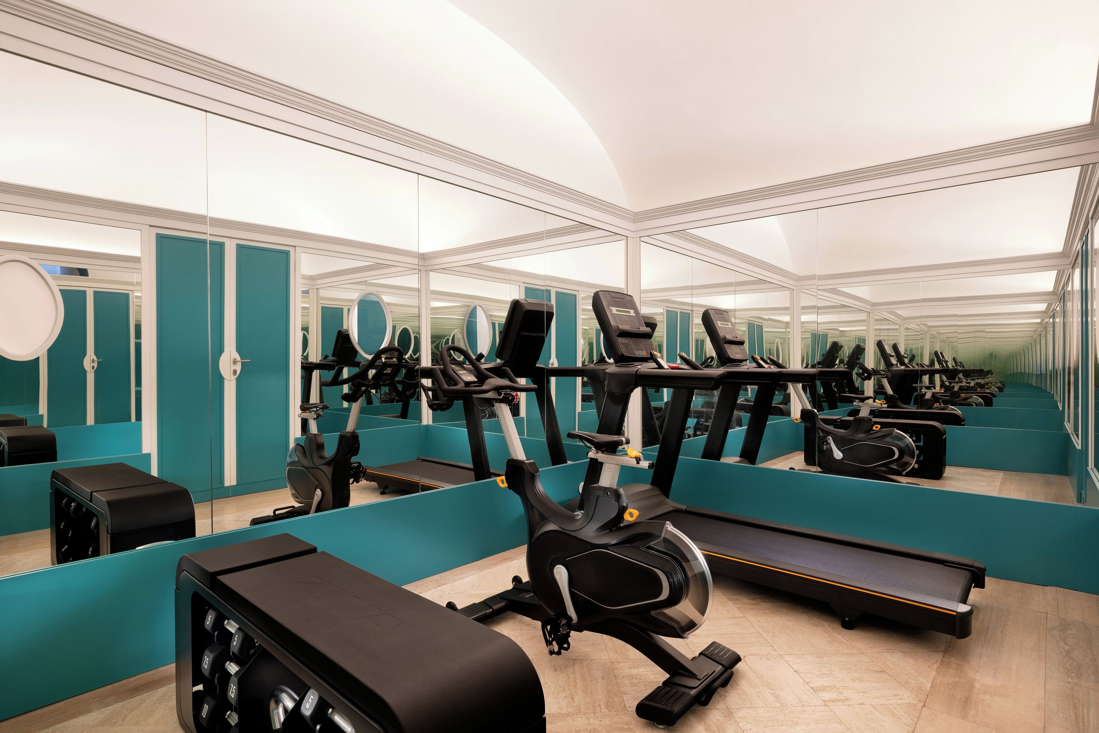 Un gimnasio con equipo de ejercicio, paredes espejadas y paredes color turquesa.