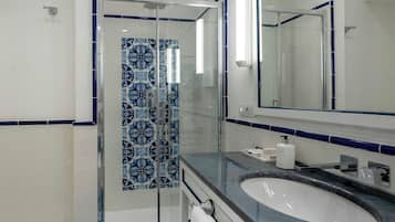 Een badkamer met een douchecabine van glas, een wit wastafelmeubel en een spiegel erboven.