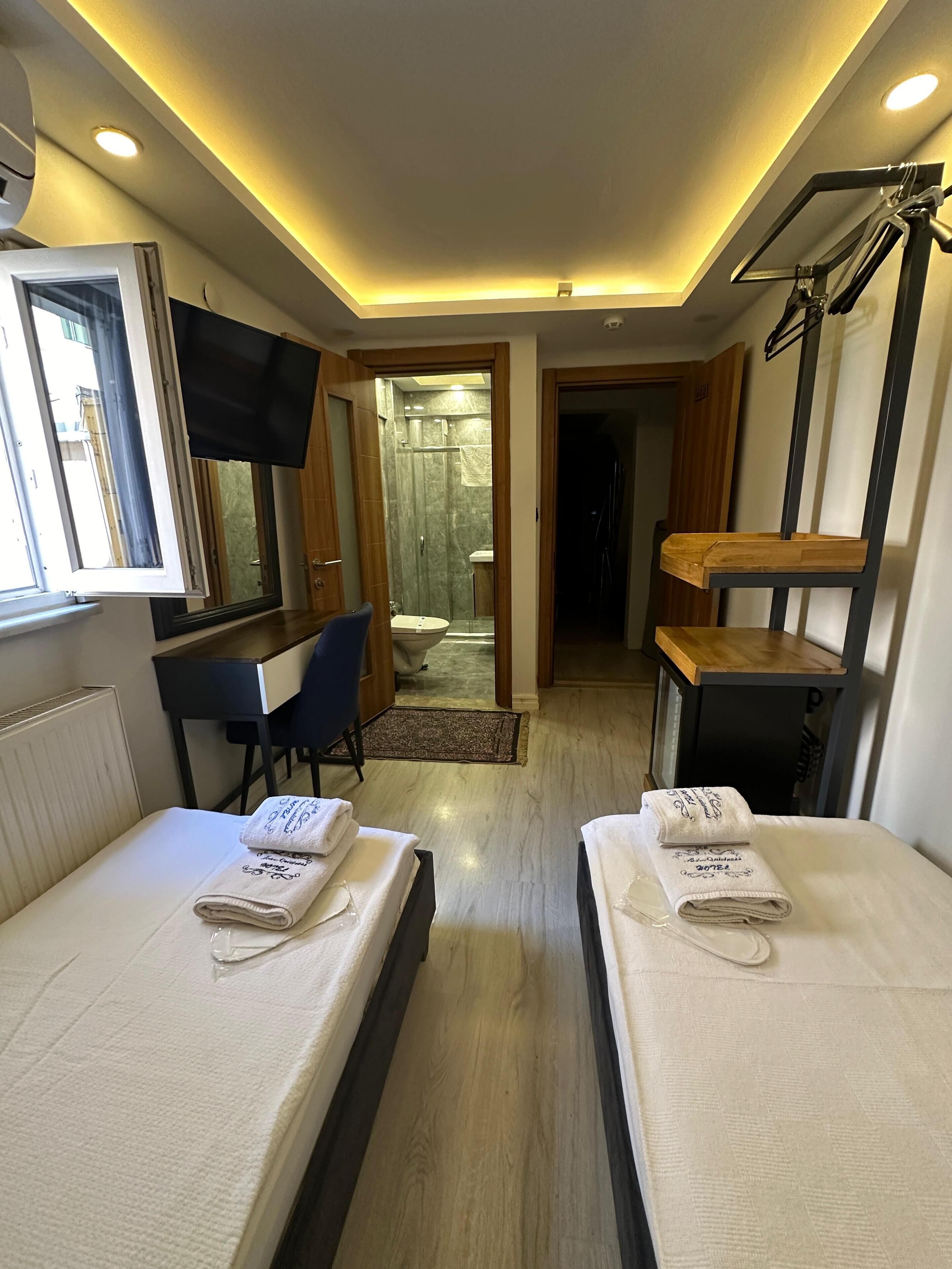 Habitació d'hotel amb dos llits, una taula de treball, una cadira, un televisor i una zona de dutxa.