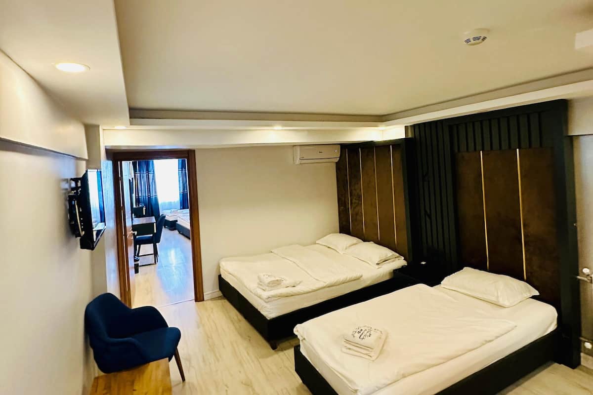 A hotel room with two beds, a desk, a chair, and a TV.