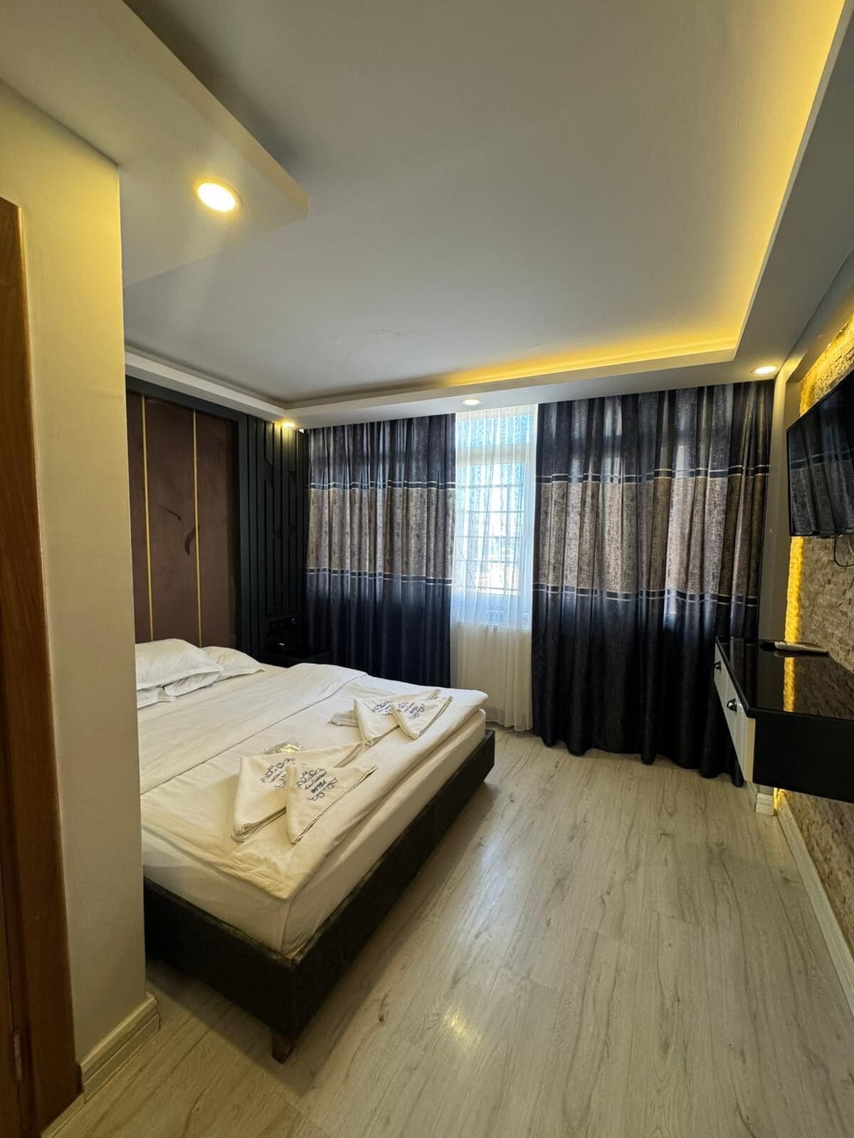Ein Schlafzimmer mit Bett, Vorhängen, Fernseher und Fenster.