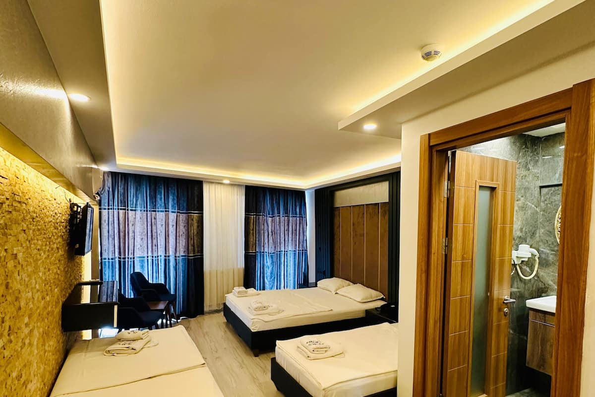 A hotel room with two beds, a desk, a chair, a small table, a bathroom with a marble wall, and a patterned rug.