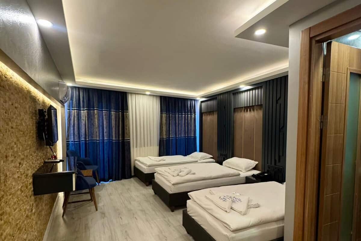 A hotel room with three beds, a desk, a chair, and a television.
