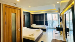 A modern hotel room with two beds, a wooden wardrobe, a dining table, and a view of the outdoor area. - Sirkeci Quietness Hotel (Istanbul)
