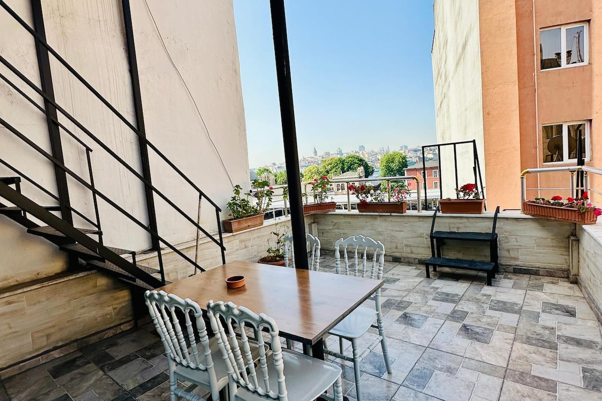 A terrace with a table and chairs, a metal railing, and a view of a cityscape.