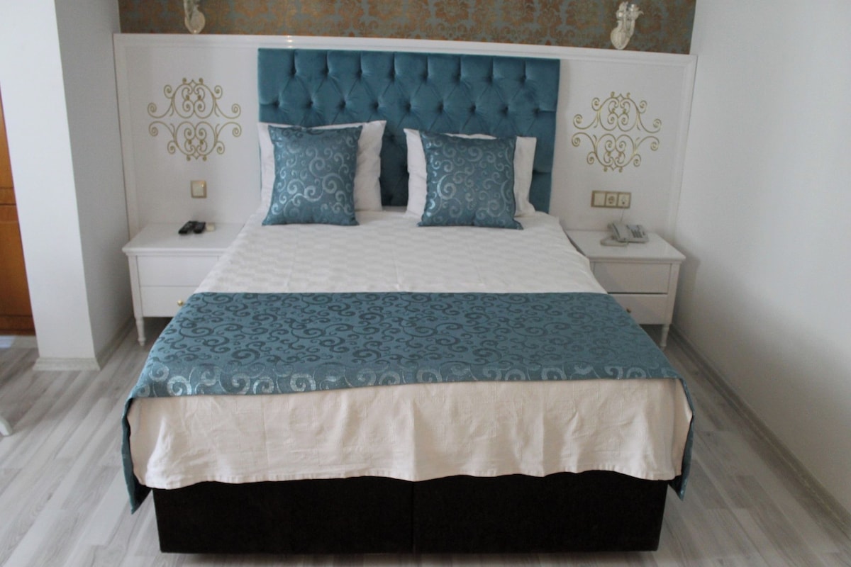 A bed with a tufted headboard, a patterned bedspread, and matching pillows. There are two bedside tables with a phone and a lamp on one.