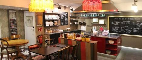 Interior de un restaurante que incluye un comedor, una cocina y una pizarra con el menú.