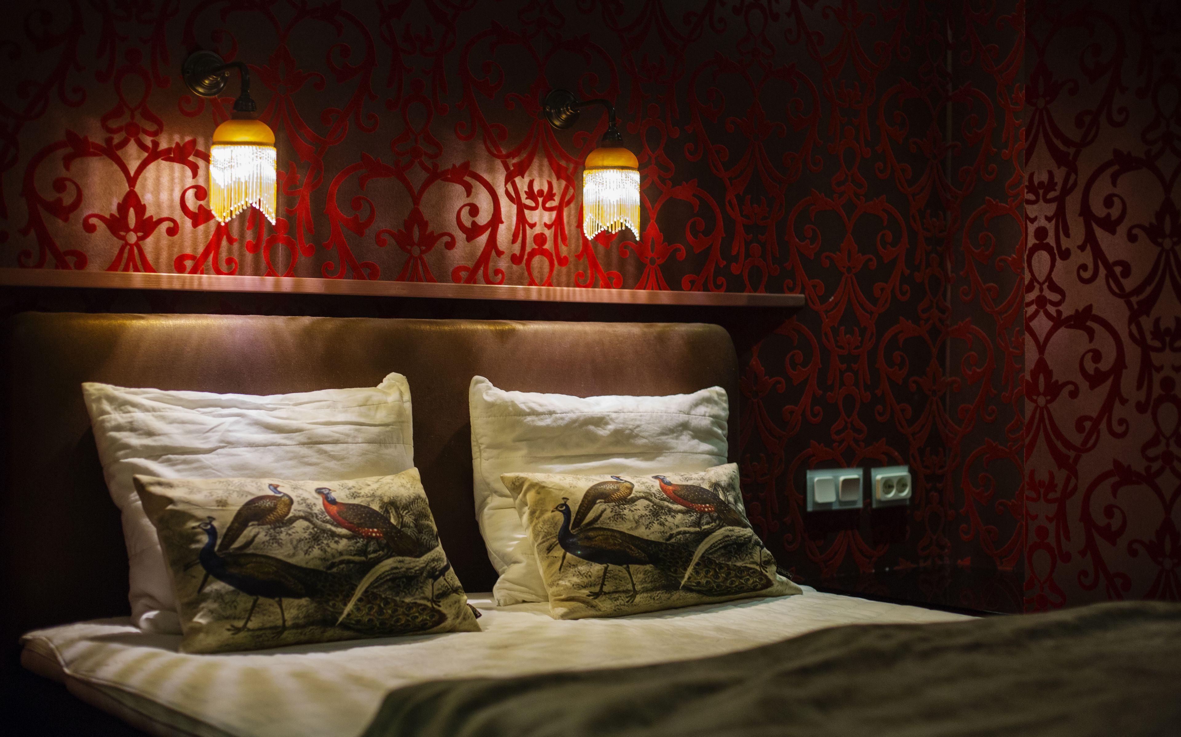Un lit avec deux oreillers, une tête de lit en bois et un mur recouvert d’un papier peint à motifs rouges.