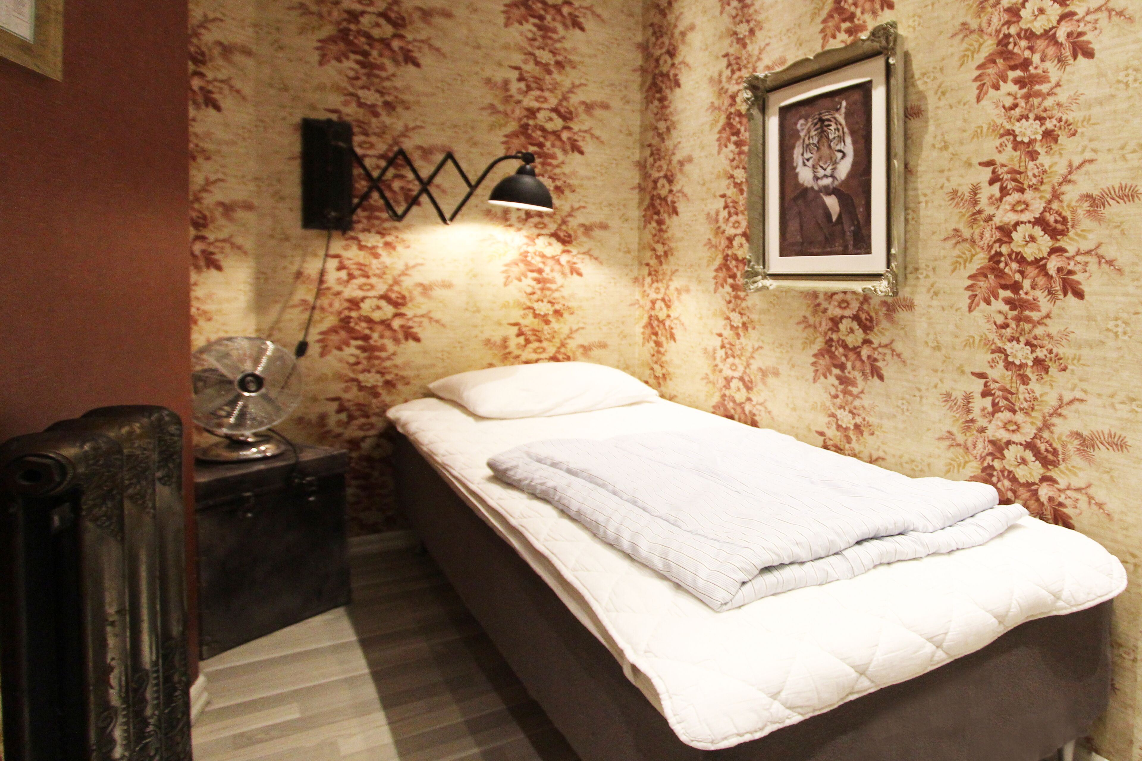 Een kleine slaapkamer met een bed, een nachtkastje, een lamp en een lijst met een afbeelding aan de muur.