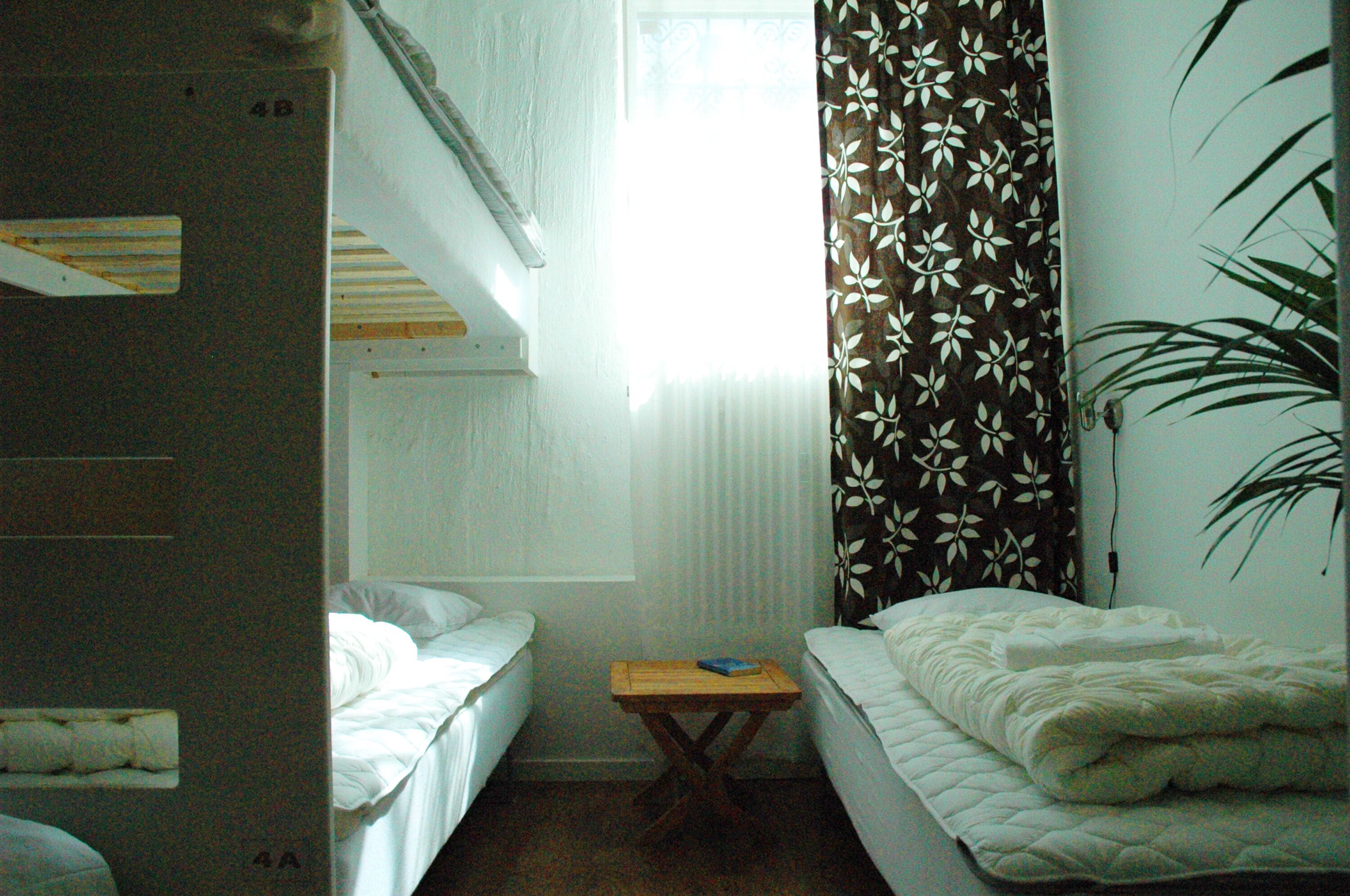 A dormitory room with bunk beds, a small table, and a window with curtains.