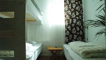 A dormitory room with bunk beds, a small table, and a window with curtains.