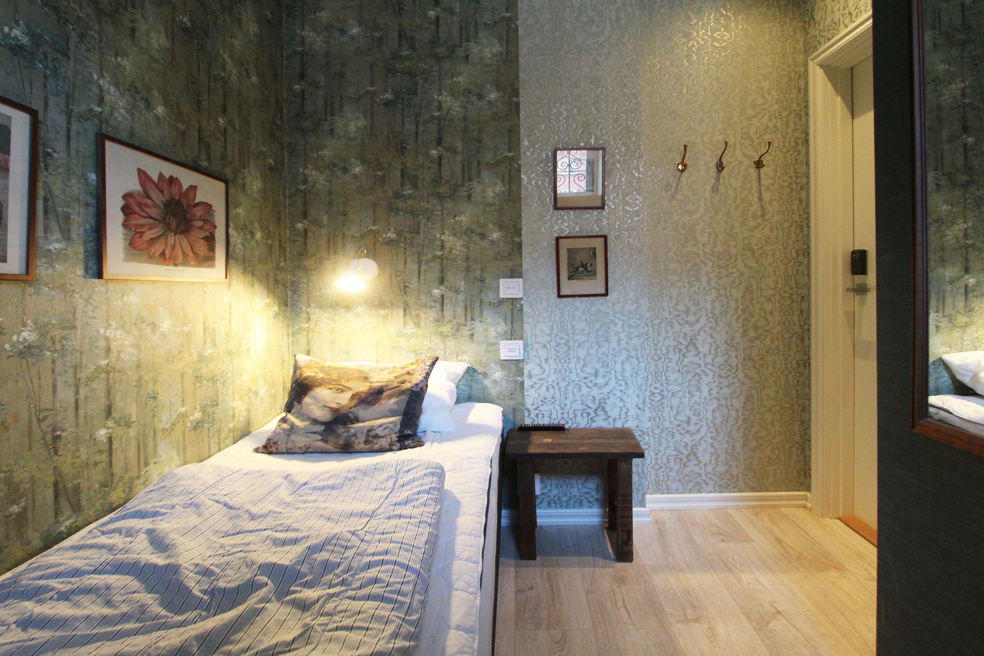 A bedroom with a bed, a bedside table, a lamp, and a wall with framed pictures.