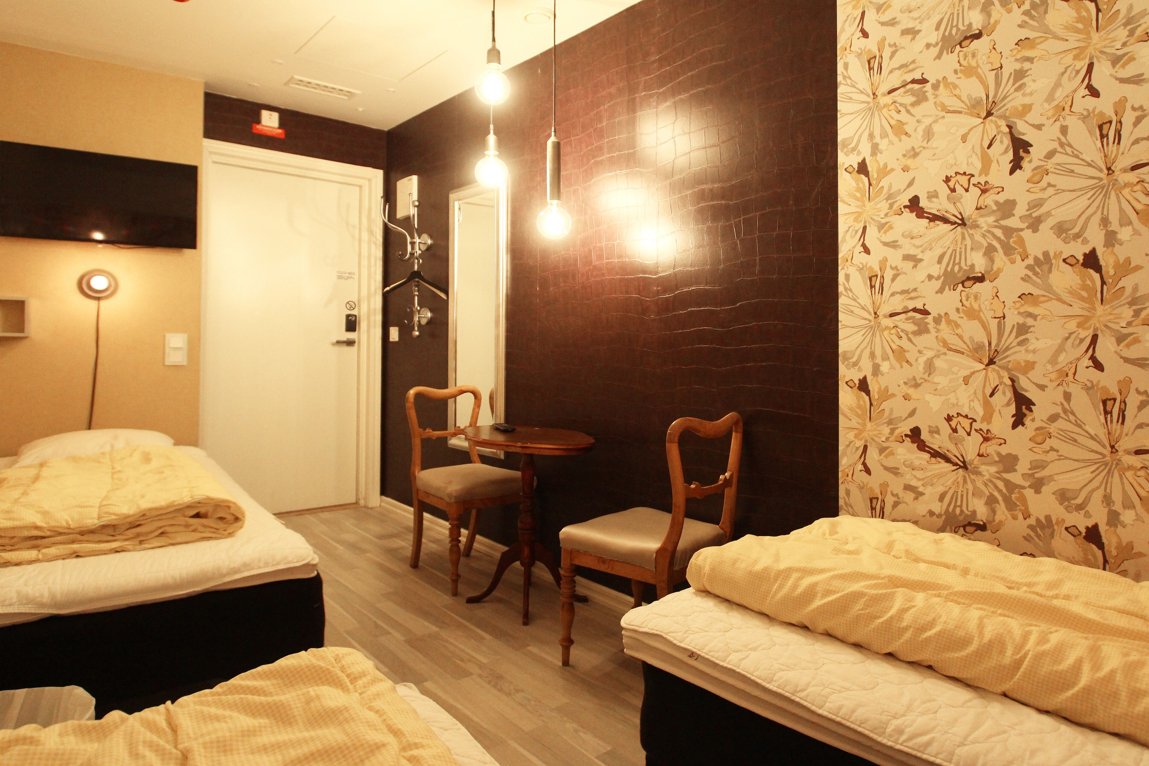 A hotel room with two beds, a small table, two chairs, and a dark wooden accent wall.