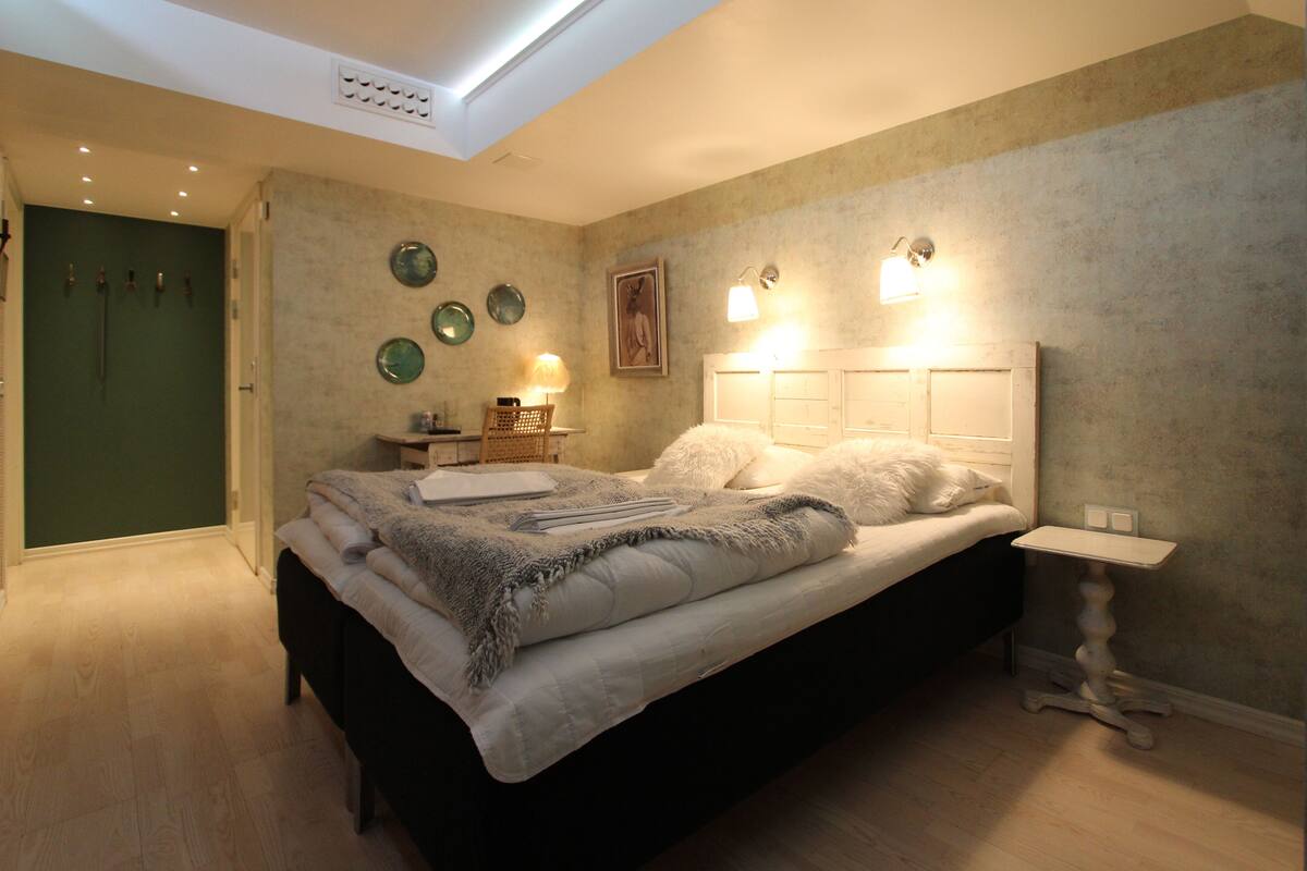 A bedroom with a bed, bedside table, lamp, and wall decor.