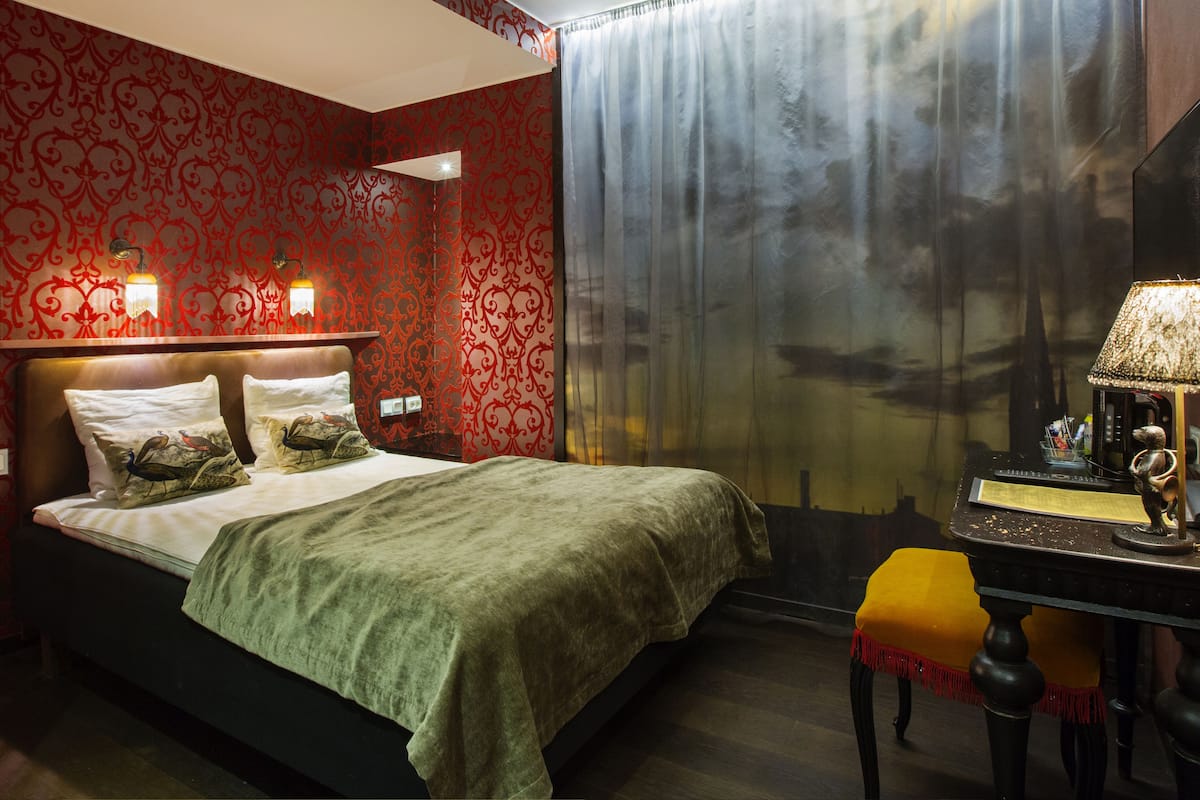 A hotel room with a bed, a desk, and a window with curtains.