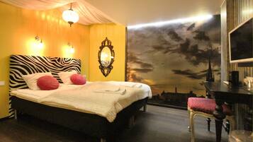 Una cama con cabecera de cebra, dos lámparas de noche y un mural de paisaje urbano en la pared.