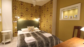 Una cama bien hecha con un edredón mullido, una mesita de noche y un espejo en la pared.