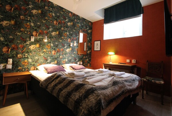 A bedroom with a floral wallpaper, a bed with a fur throw, a nightstand, a chair, and a window with a black valance. - Skanstulls Boutique Hostel (Stockholm)